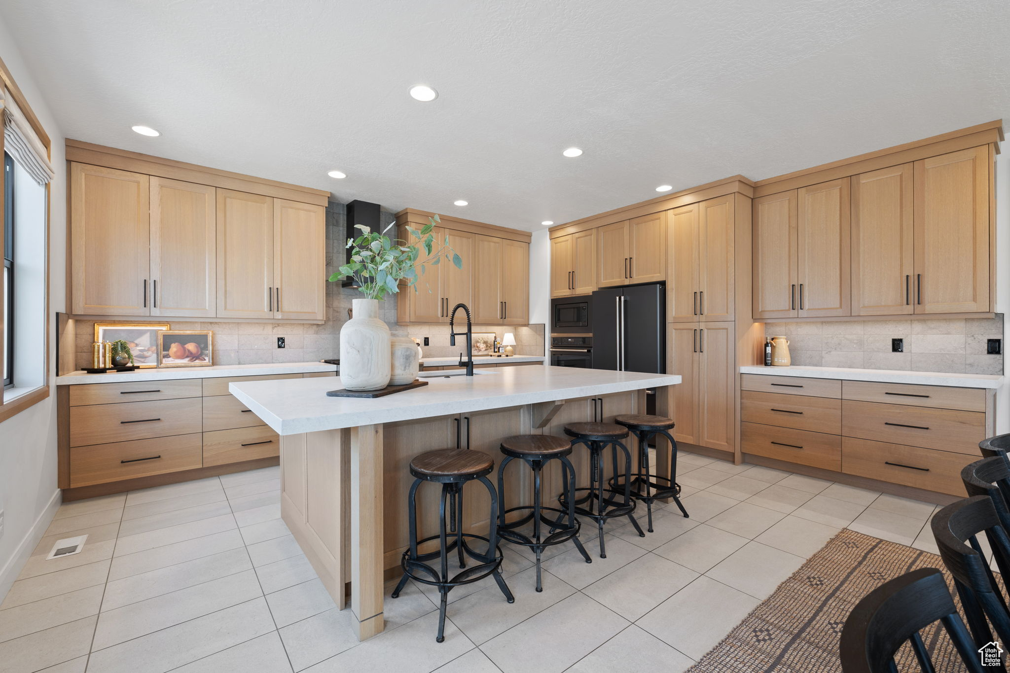 Kitchen with a center island with sink, black appliances, a breakfast bar area, and tasteful backsplash