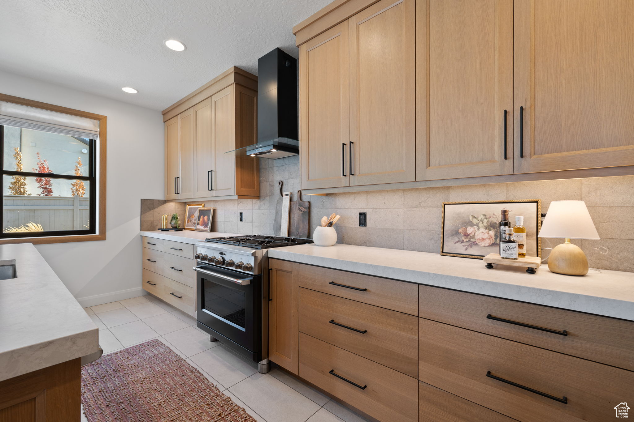 Kitchen featuring tasteful backsplash, wall chimney exhaust hood, light tile patterned floors, light brown cabinets, and high end stainless steel range