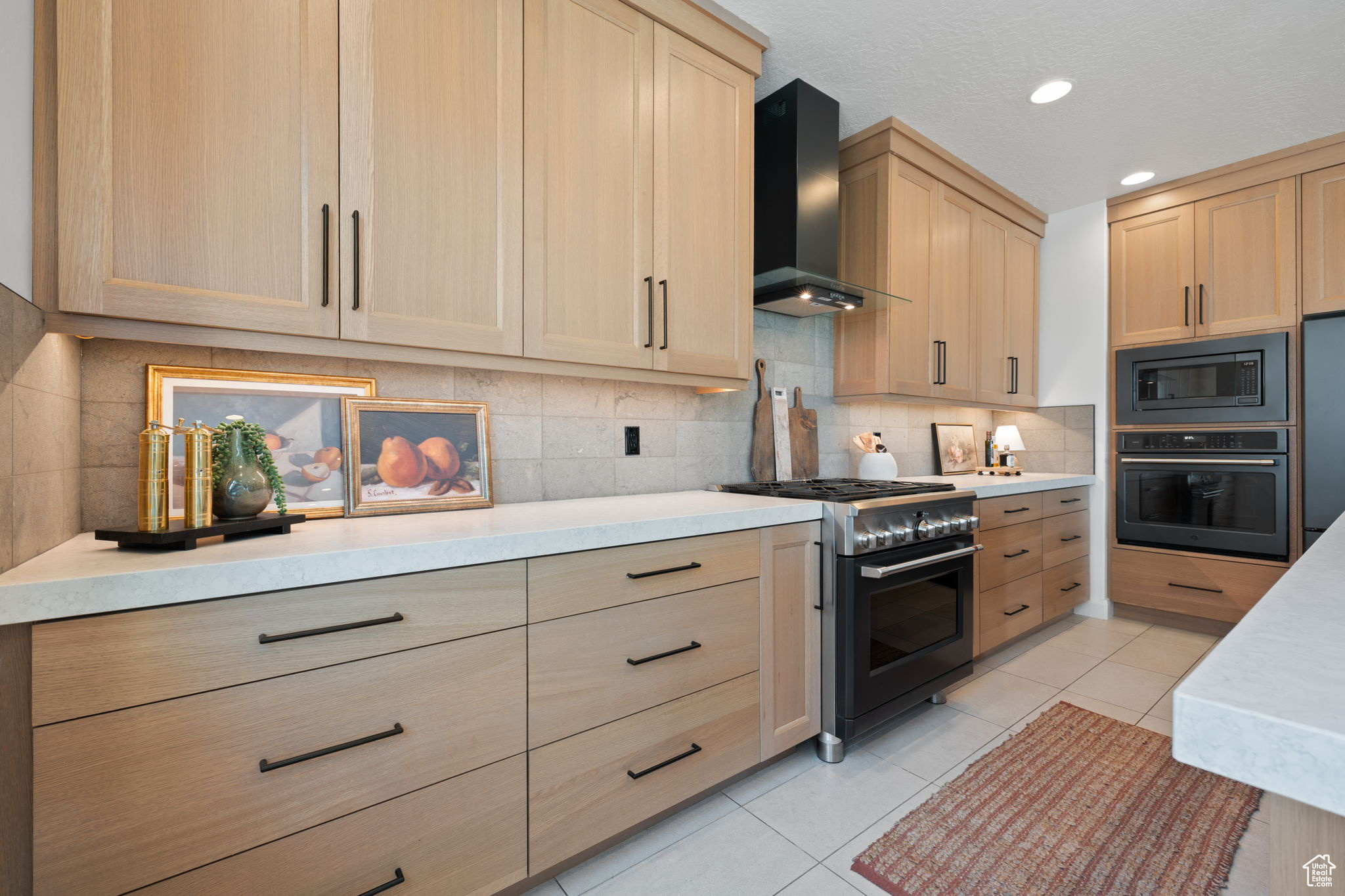 Kitchen with light brown cabinets, light tile patterned floors, stainless steel appliances, and wall chimney range hood