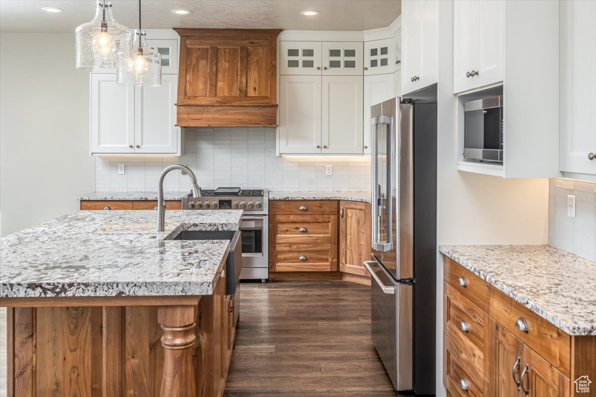 Kitchen with white cabinetry, a center island with sink, and high end appliances