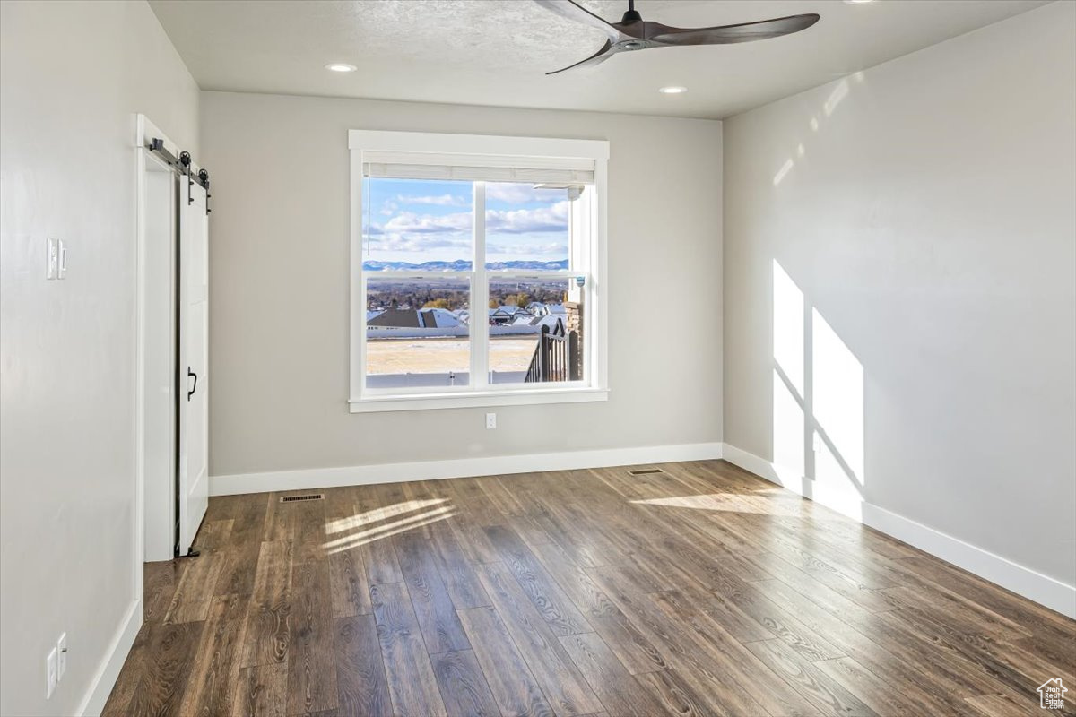 Interior space with a barn door, ceiling fan, and dark wood-type flooring