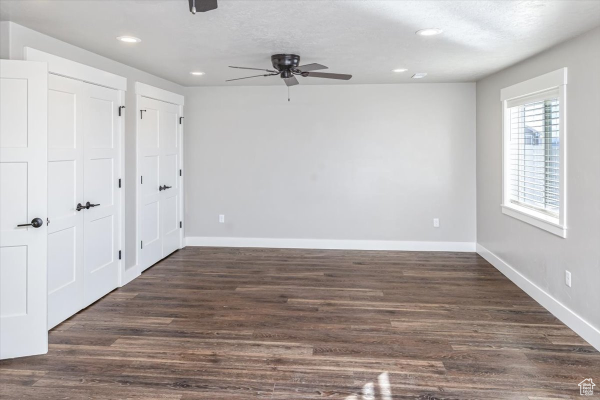 Unfurnished bedroom with ceiling fan, dark hardwood / wood-style flooring, a textured ceiling, and two closets