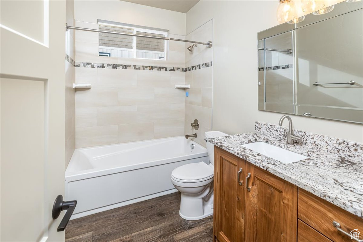 Full bathroom with vanity, toilet, wood-type flooring, and tiled shower / bath