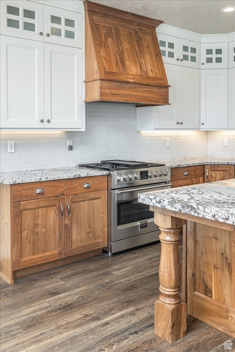 Kitchen with premium range hood, dark wood-type flooring, light stone countertops, stainless steel range, and white cabinetry