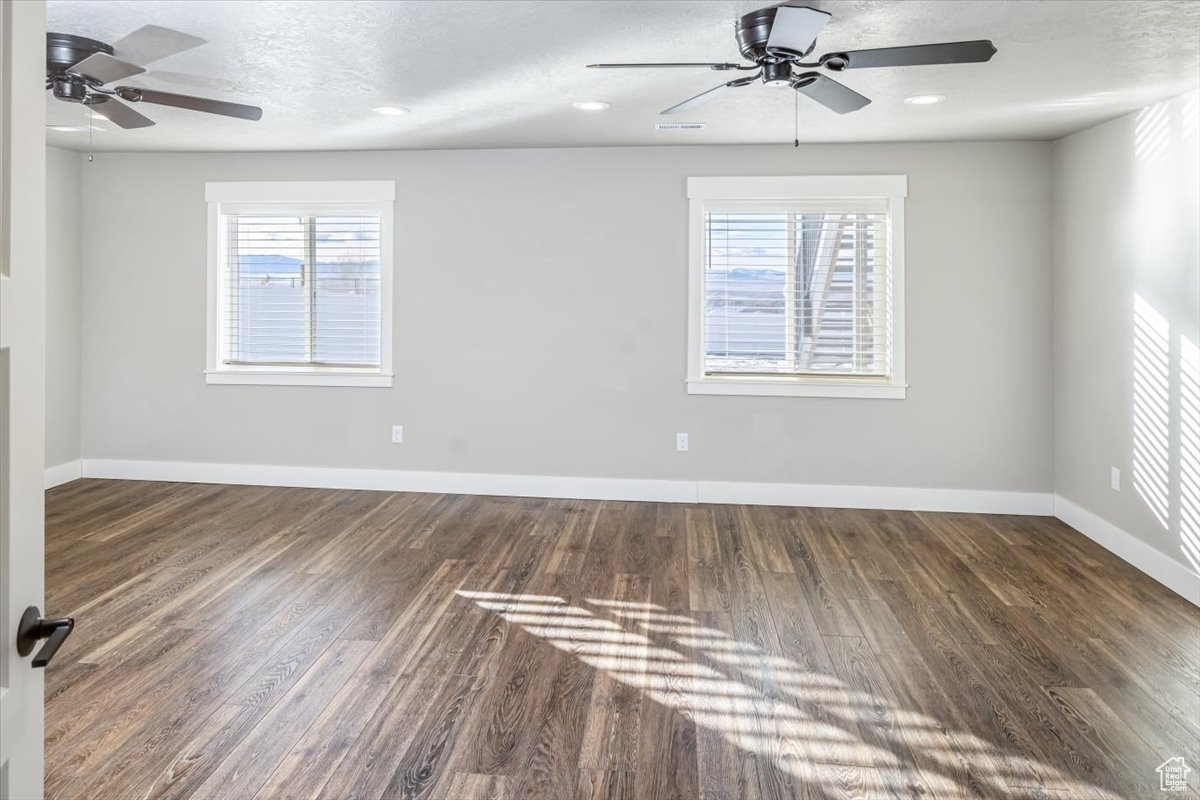 Spare room featuring a textured ceiling, ceiling fan, dark wood-type flooring, and a wealth of natural light