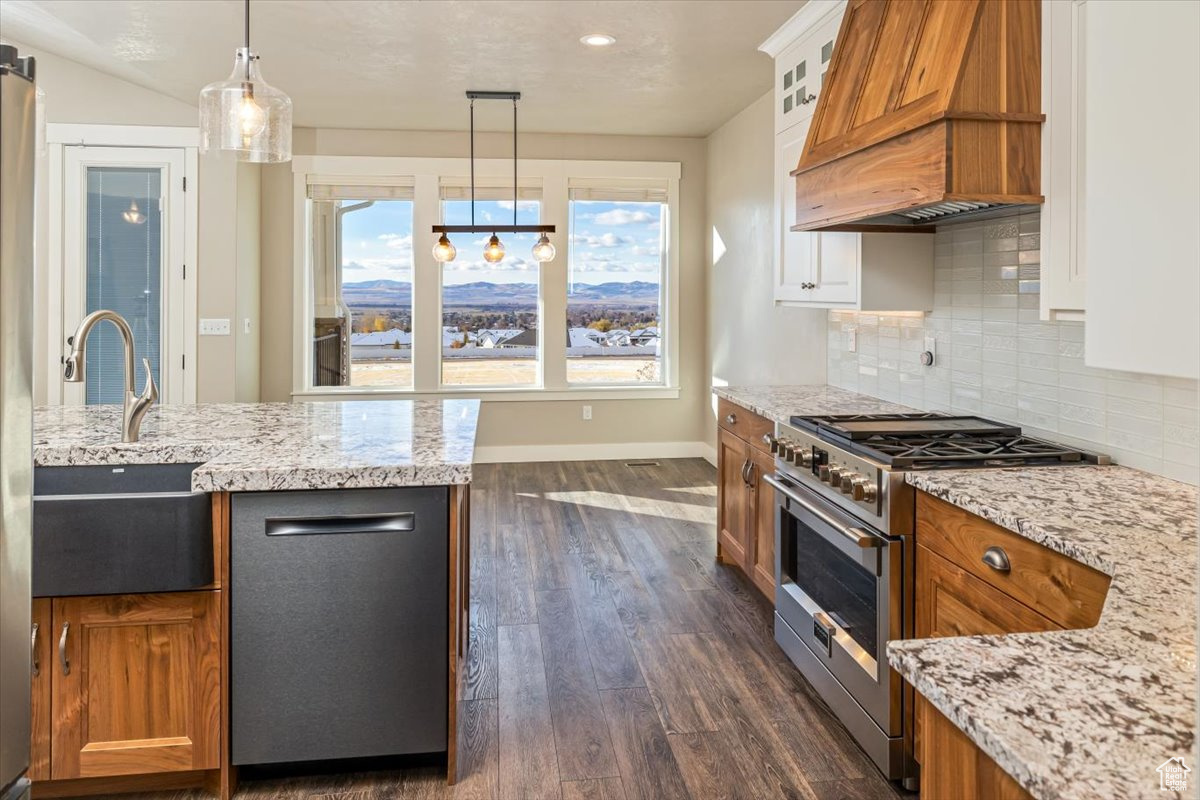 Kitchen featuring light stone countertops, custom range hood, stainless steel appliances, decorative light fixtures, and dark hardwood / wood-style floors