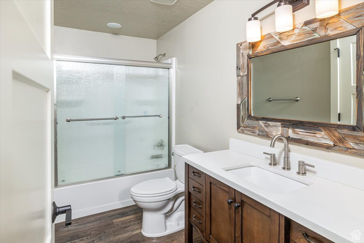 Full bathroom featuring enclosed tub / shower combo, wood-type flooring, a textured ceiling, toilet, and vanity