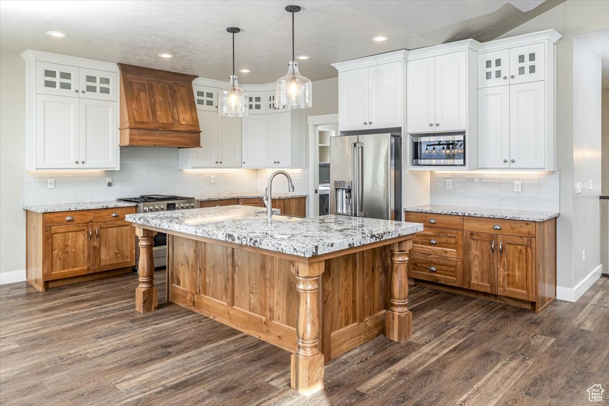 Kitchen with white cabinetry, a center island with sink, and high end appliances