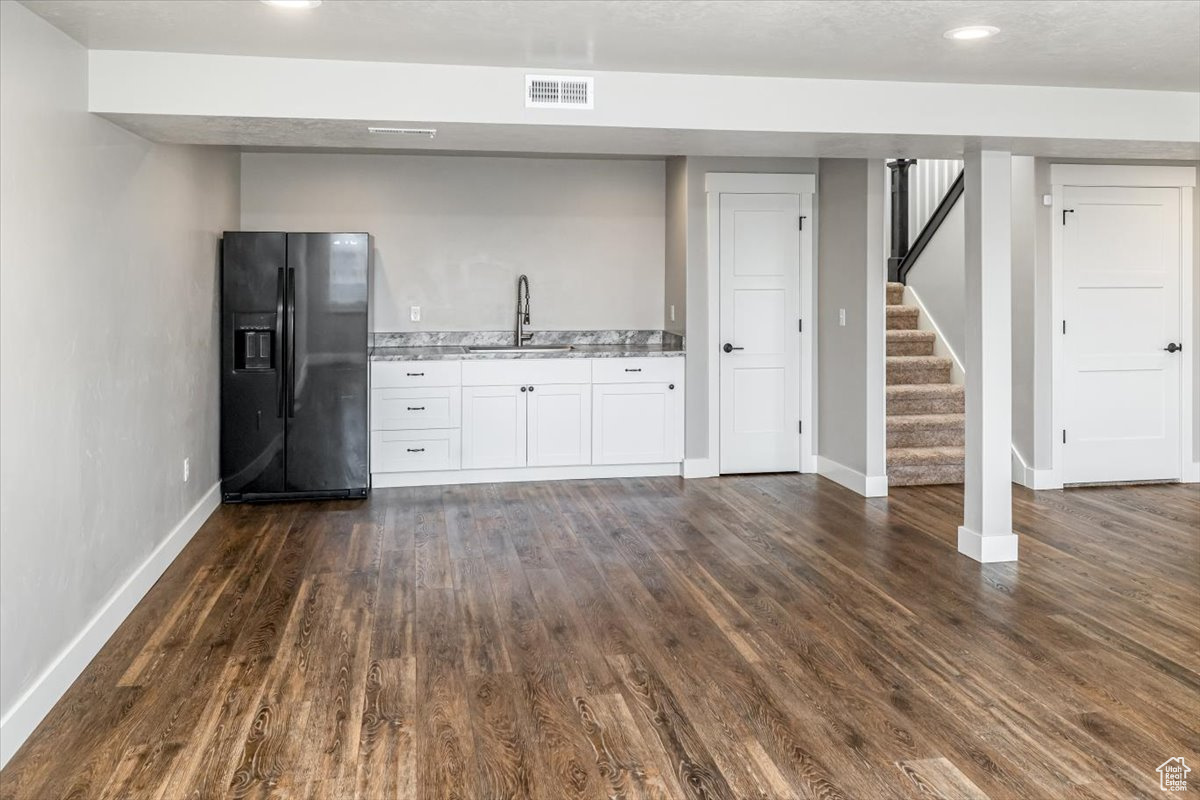 Kitchen with light stone countertops, black fridge, dark wood-type flooring, sink, and white cabinetry