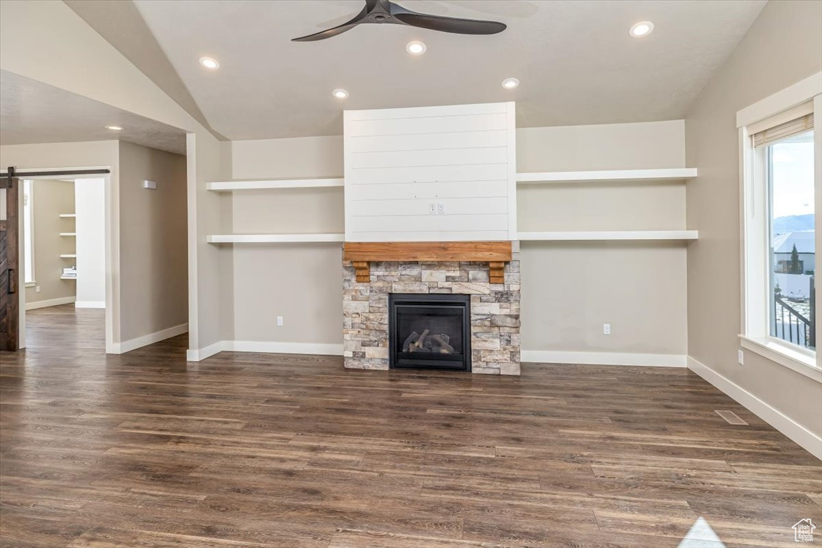 Unfurnished living room featuring a stone fireplace, ceiling fan, dark hardwood / wood-style floors, and vaulted ceiling