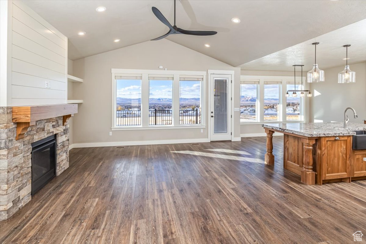 Interior space featuring decorative light fixtures, a center island with sink, a fireplace, dark hardwood / wood-style floors, and lofted ceiling