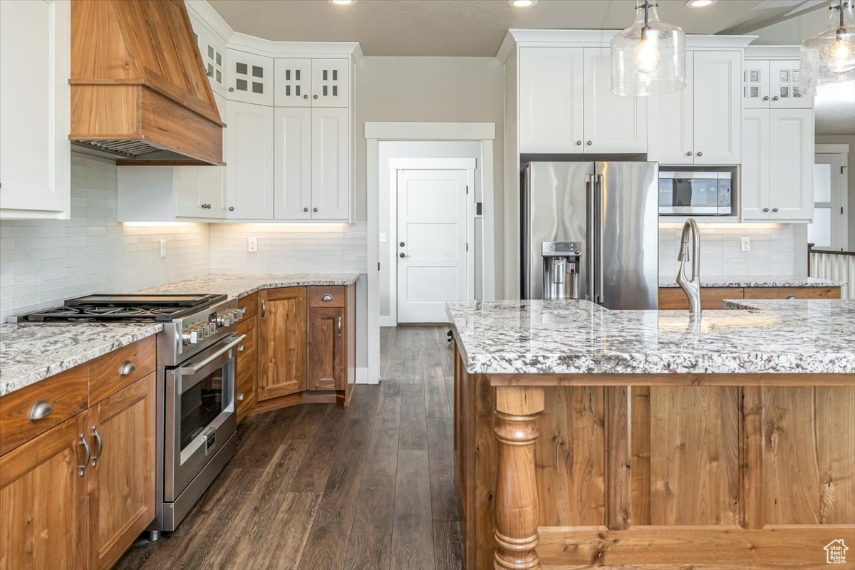 Kitchen with pendant lighting, premium range hood, premium appliances, dark hardwood / wood-style flooring, and white cabinetry