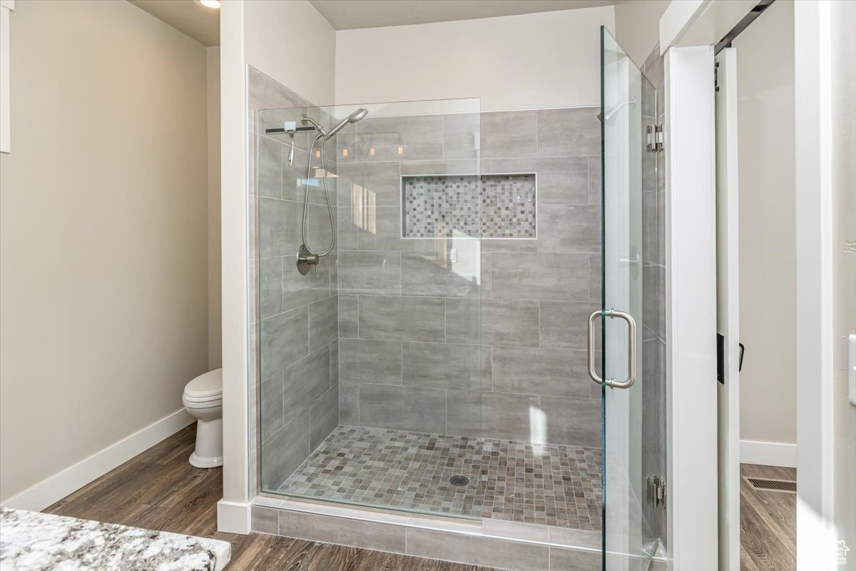 Bathroom with hardwood / wood-style flooring, toilet, and a shower with door