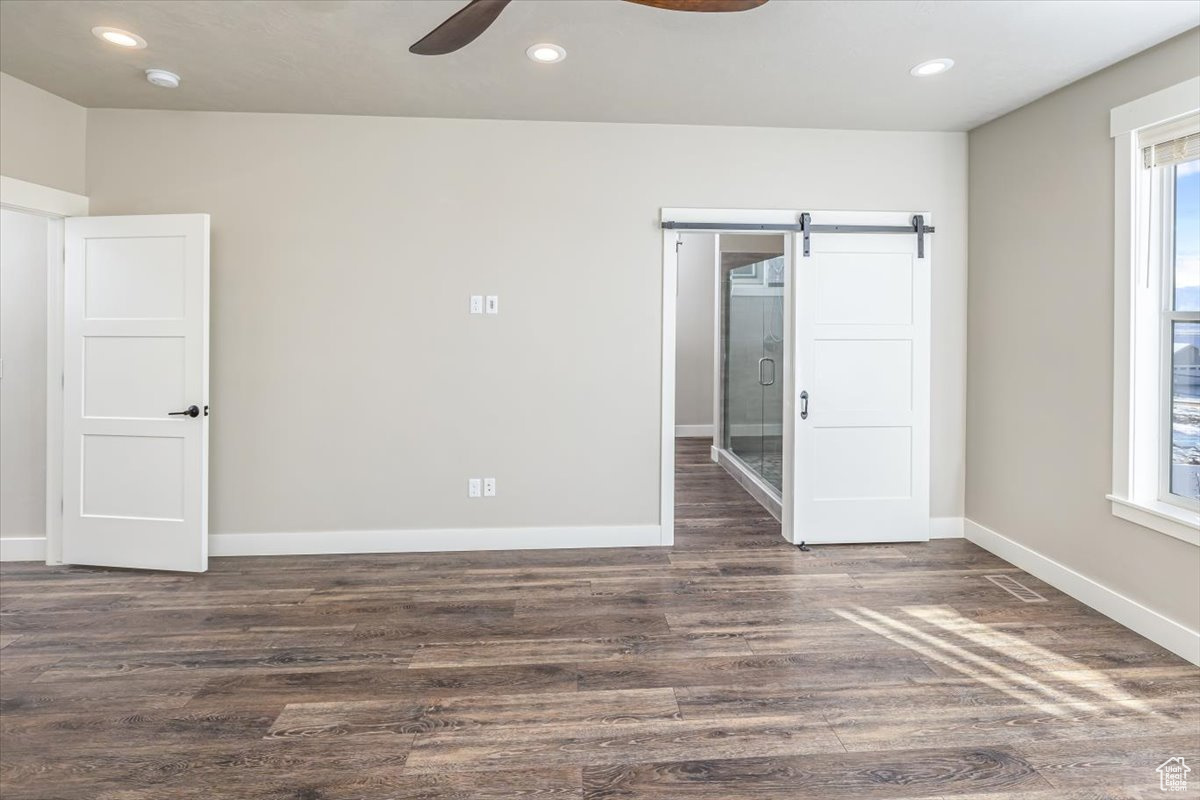 Spare room with a barn door, ceiling fan, and dark hardwood / wood-style floors