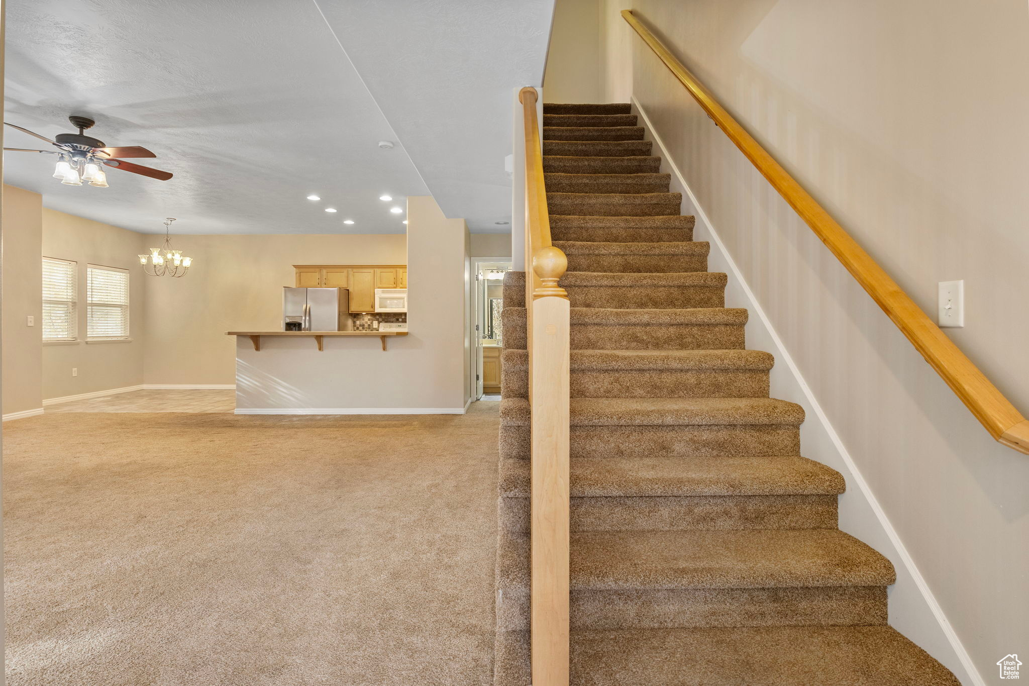 Staircase featuring ceiling fan with notable chandelier and carpet floors