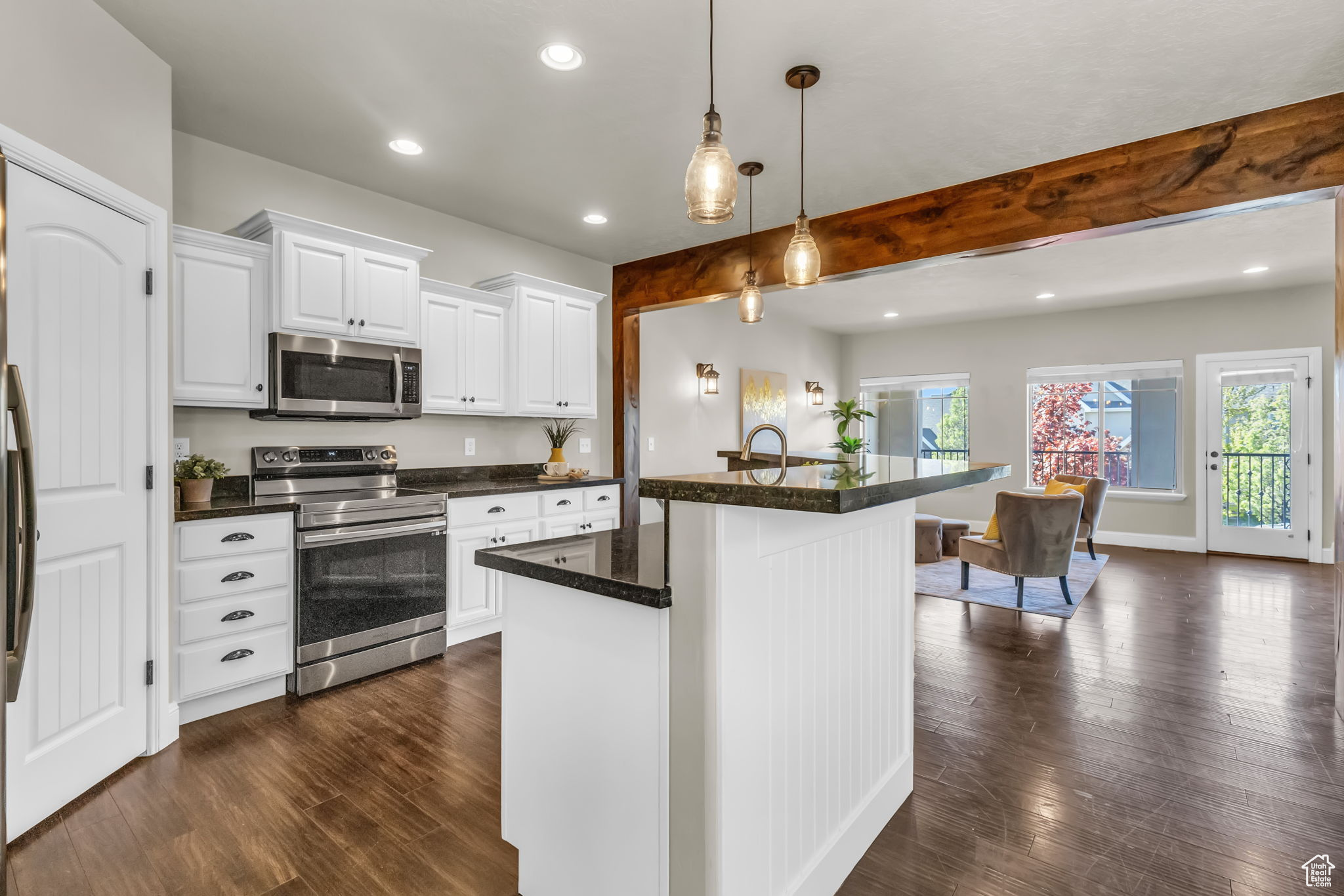 Kitchen with dark wood-type flooring, hanging light fixtures, a kitchen island, white cabinetry, and stainless steel appliances