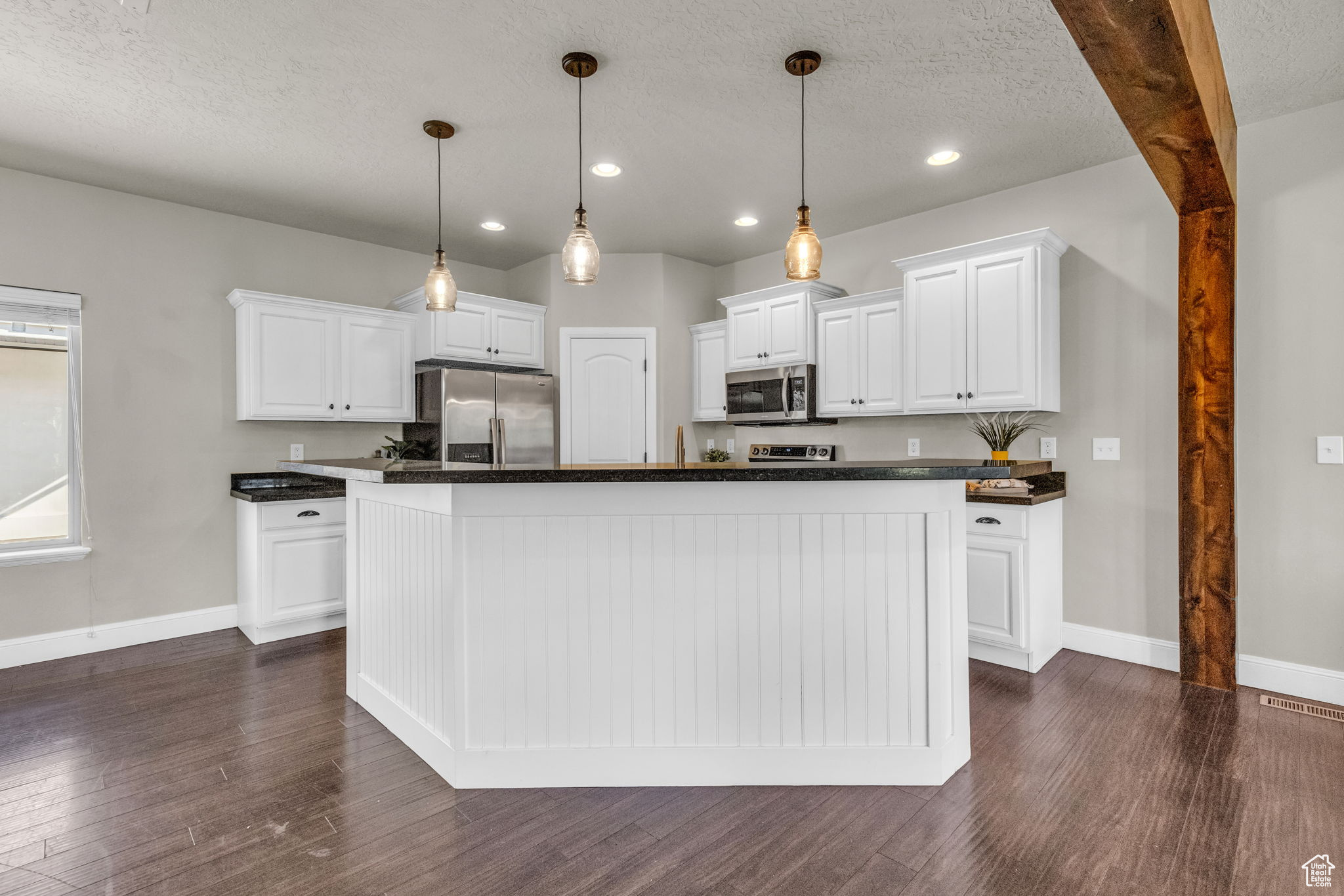 Kitchen with appliances with stainless steel finishes, dark hardwood / wood-style flooring, pendant lighting, white cabinets, and a center island