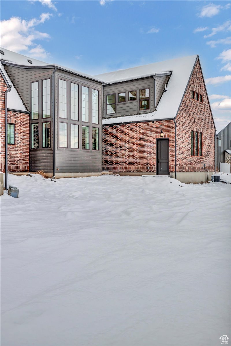 Snow covered back of property featuring cooling unit