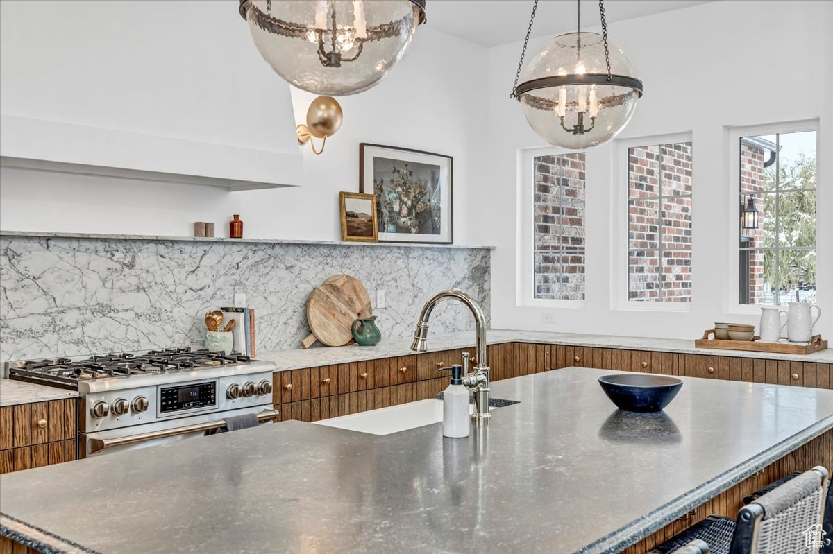 Kitchen with decorative backsplash, high end stove, sink, decorative light fixtures, and a center island