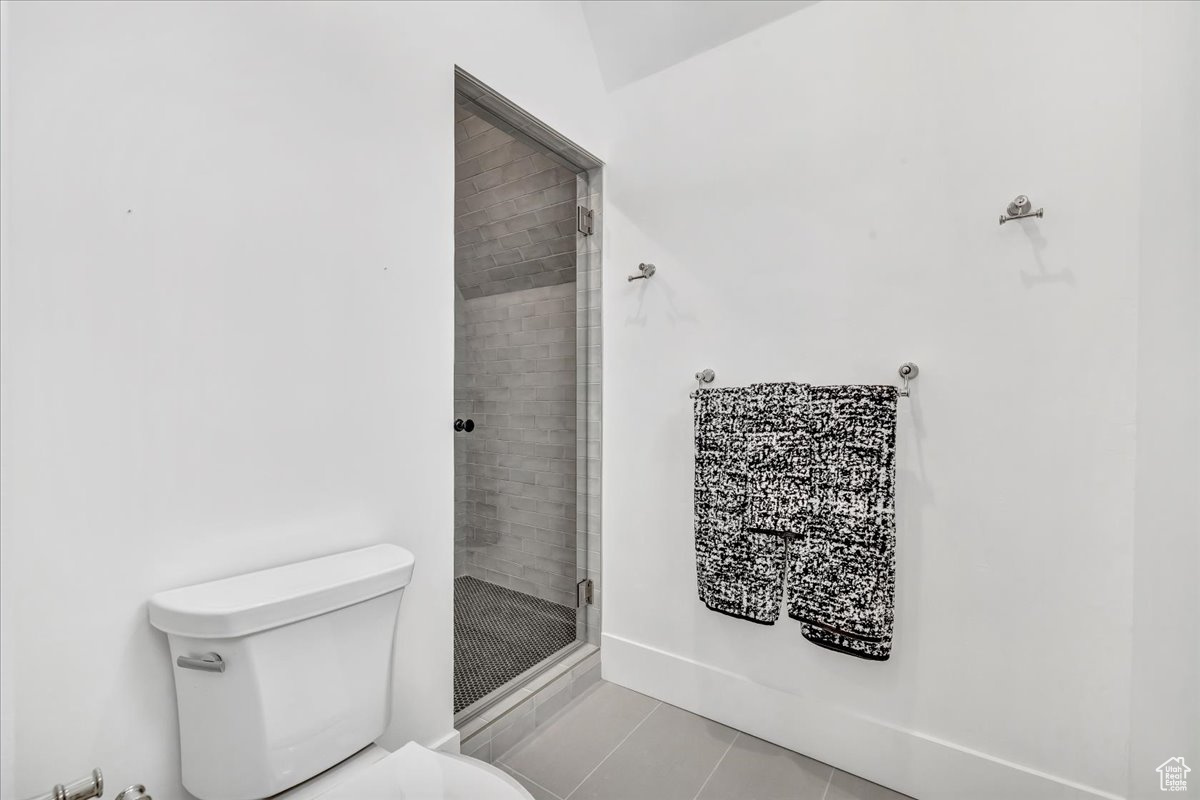 Bathroom with tile patterned flooring, lofted ceiling, toilet, and a shower with shower door