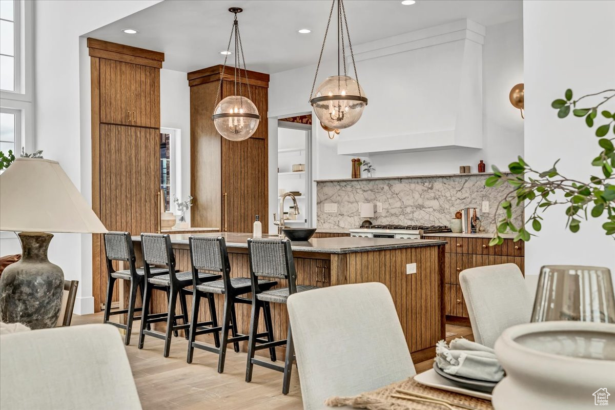 Kitchen with pendant lighting, backsplash, light wood-type flooring, a notable chandelier, and kitchen peninsula