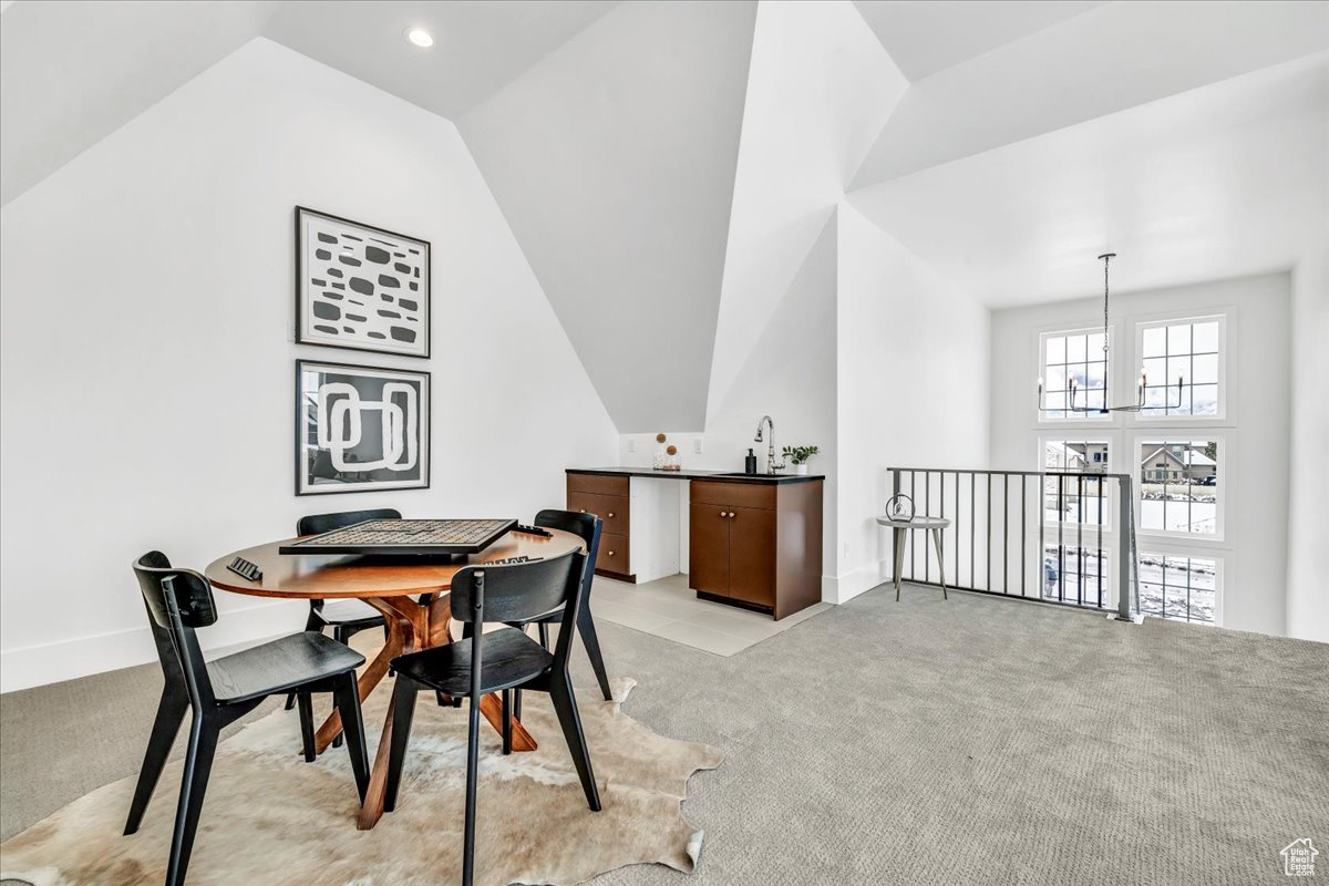 Dining area featuring lofted ceiling, light carpet, and an inviting chandelier