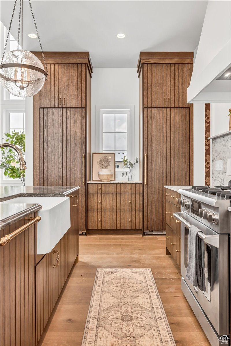 Kitchen featuring custom exhaust hood, decorative light fixtures, high end stainless steel range, light wood-type flooring, and a notable chandelier