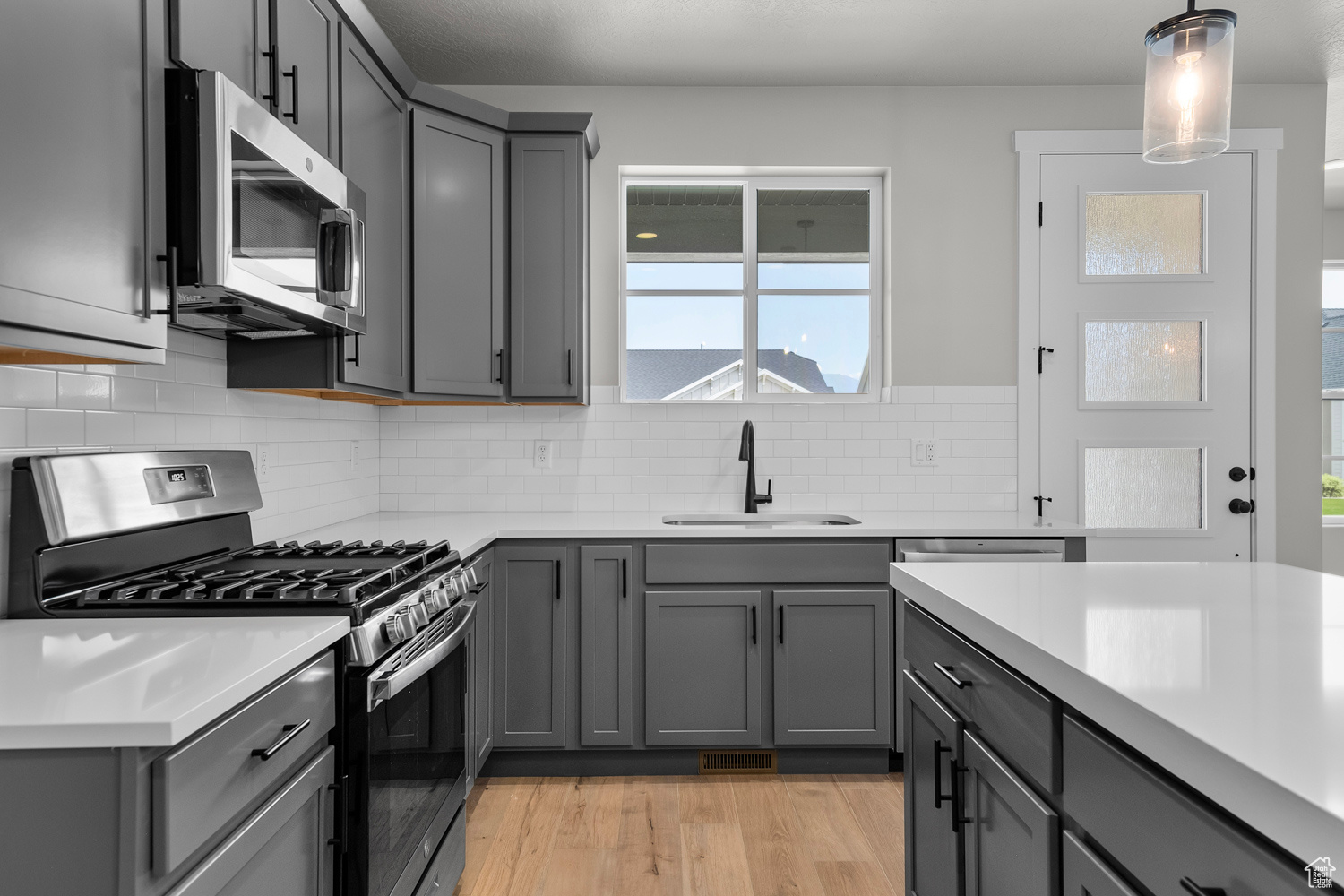 Kitchen featuring gray cabinetry, sink, hanging light fixtures, stainless steel appliances, and light wood-type flooring