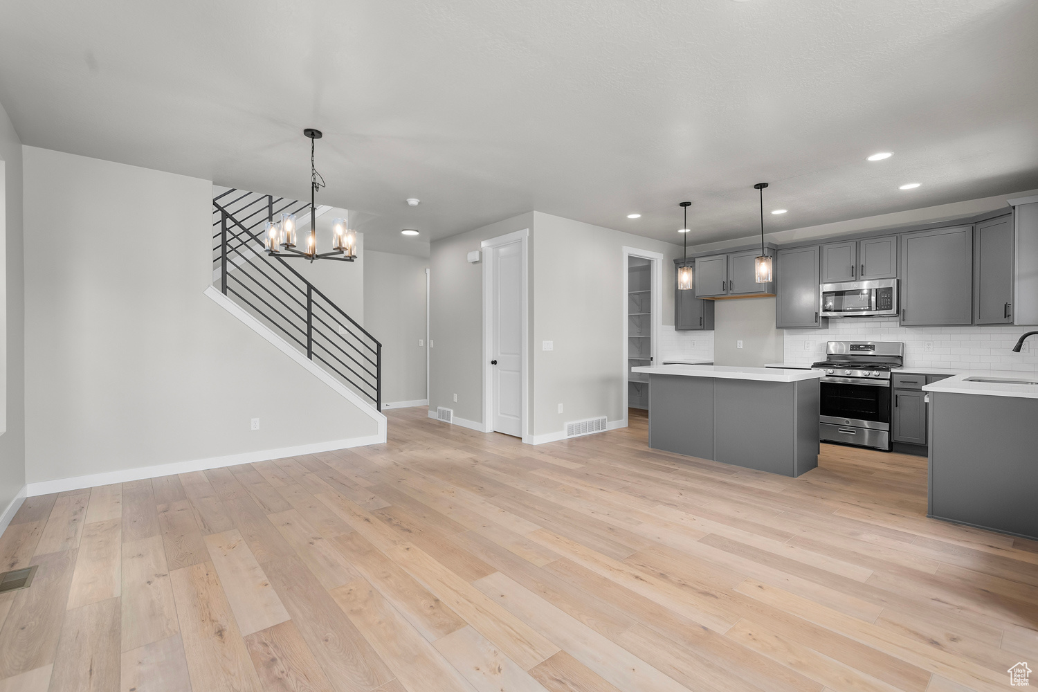 Kitchen featuring appliances with stainless steel finishes, a center island, gray cabinets, and hanging light fixtures