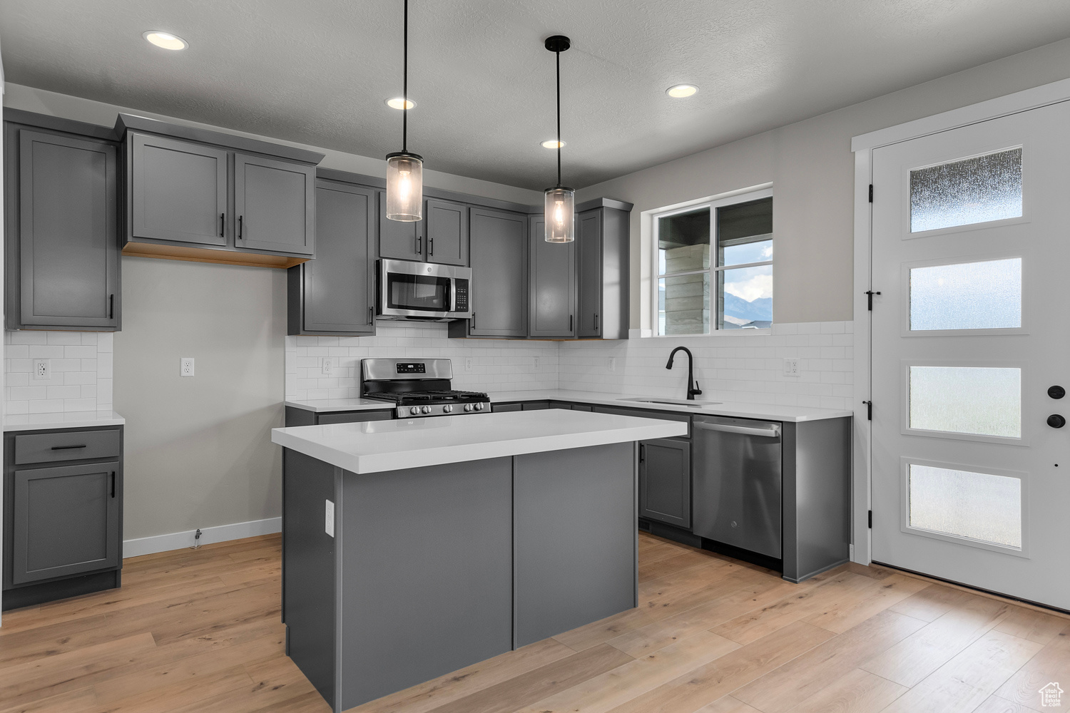 Kitchen featuring gray cabinetry, a center island, hanging light fixtures, appliances with stainless steel finishes, and light wood-type flooring