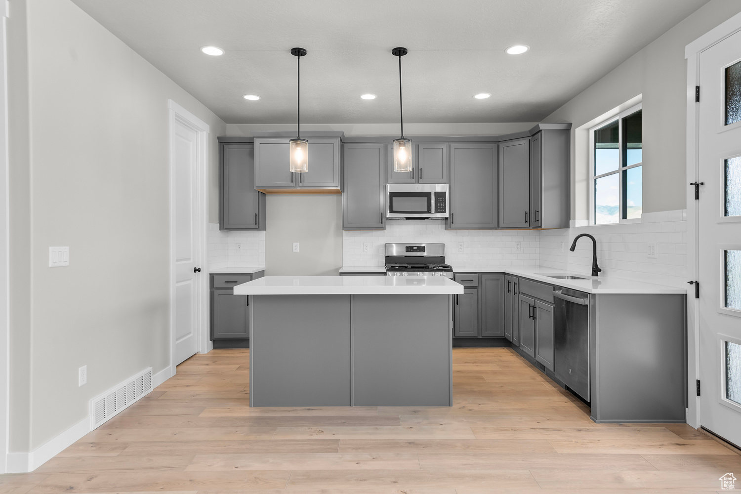 Kitchen featuring appliances with stainless steel finishes, gray cabinetry, sink, a center island, and light hardwood / wood-style floors