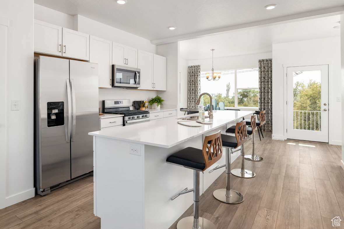 Kitchen with white cabinets, stainless steel appliances, a kitchen island with sink, and light hardwood / wood-style floors