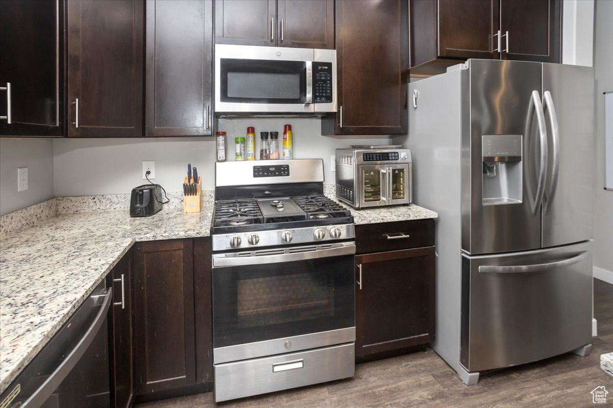 Kitchen with dark brown cabinetry, light stone countertops, dark wood-type flooring, and stainless steel appliances