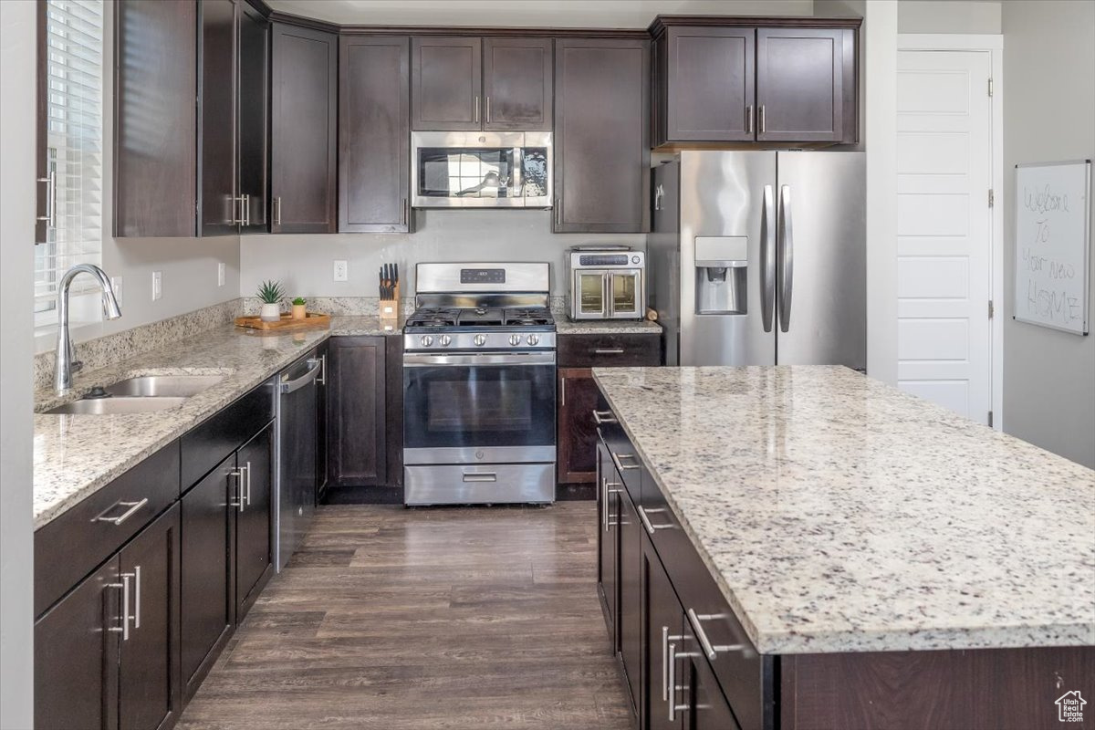 Kitchen featuring light stone countertops, sink, a center island, stainless steel appliances, and dark hardwood / wood-style flooring