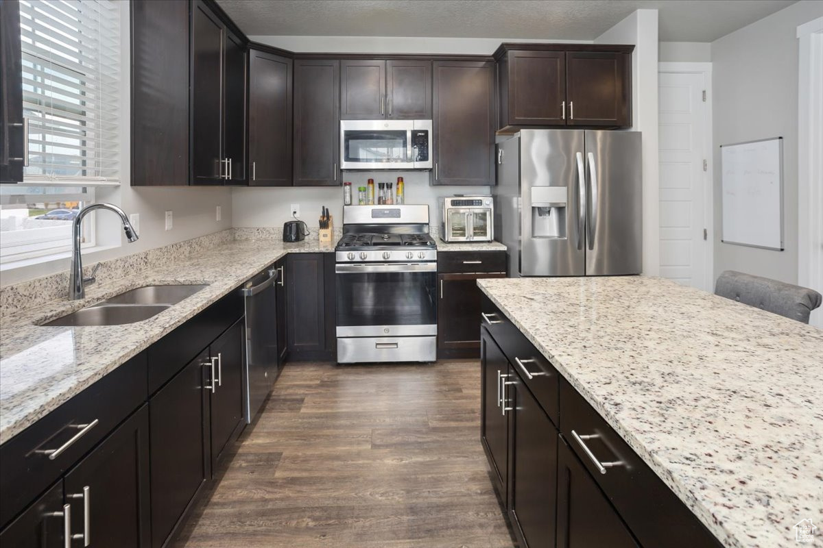 Kitchen featuring appliances with stainless steel finishes, light stone counters, dark brown cabinets, sink, and dark hardwood / wood-style floors