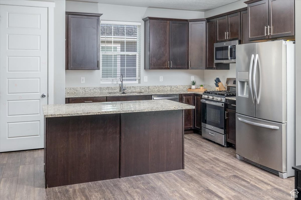 Kitchen with sink, a center island, stainless steel appliances, dark brown cabinets, and light wood-type flooring