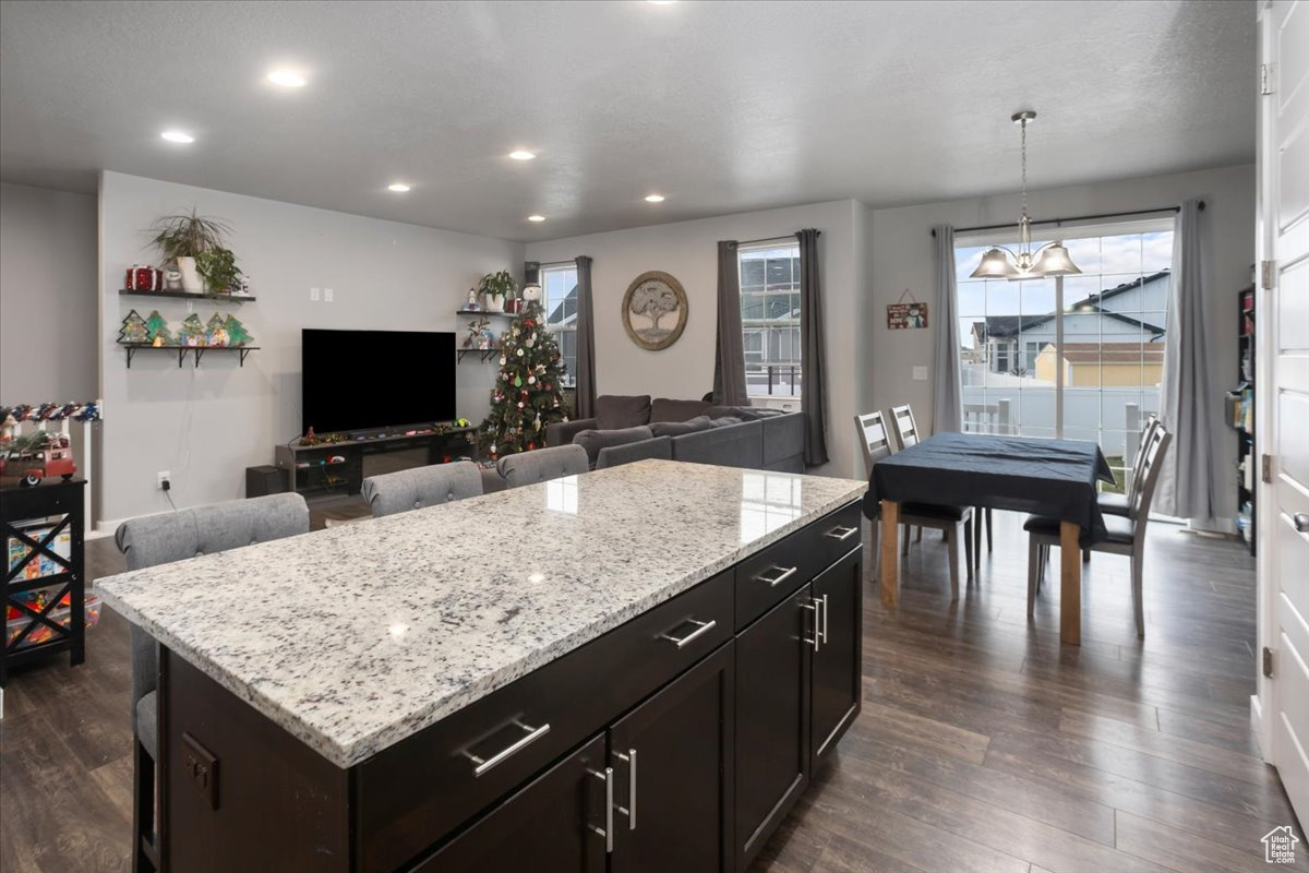 Kitchen with dark wood-type flooring, an inviting chandelier, decorative light fixtures, dark brown cabinets, and a kitchen island