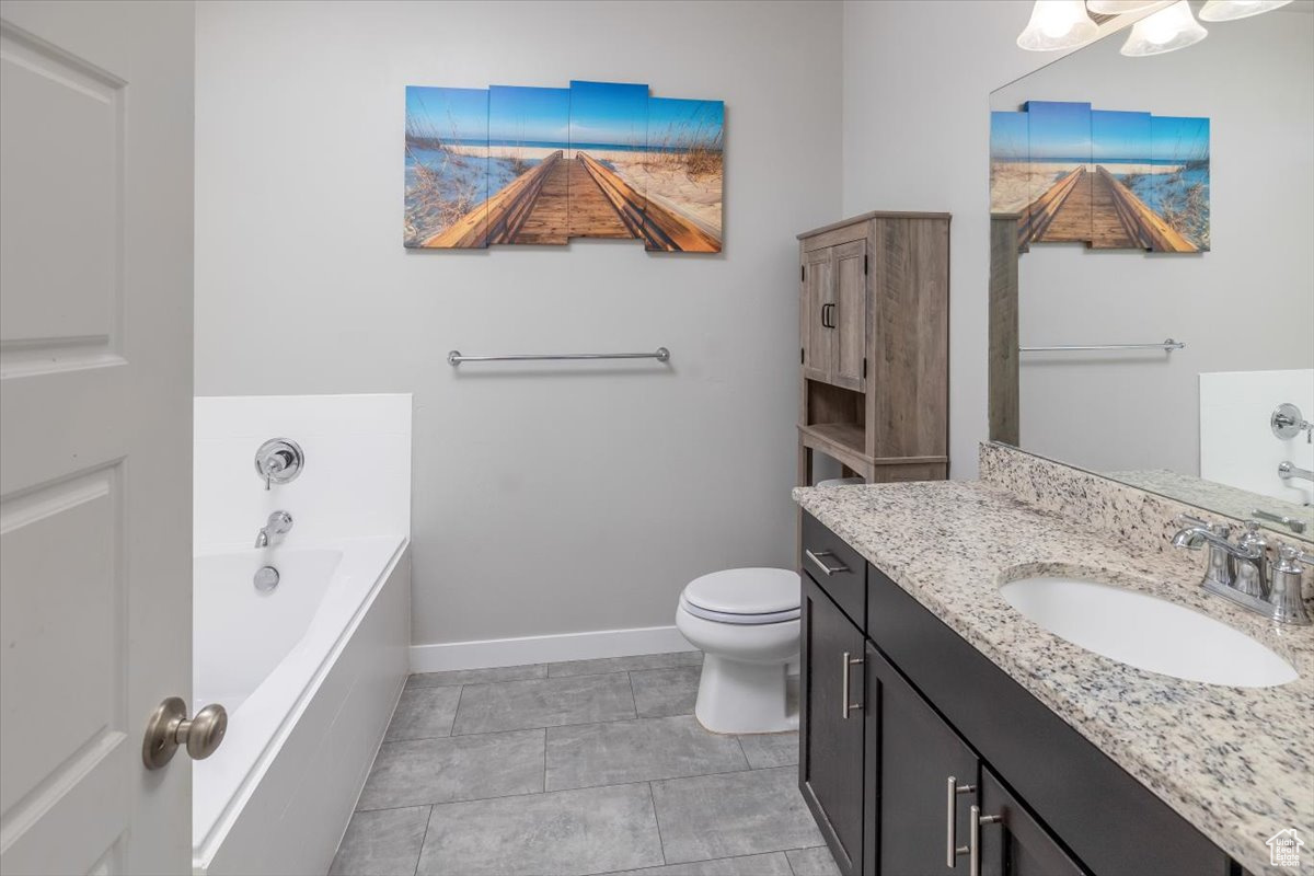 Bathroom featuring tile patterned floors, vanity, toilet, and a tub to relax in