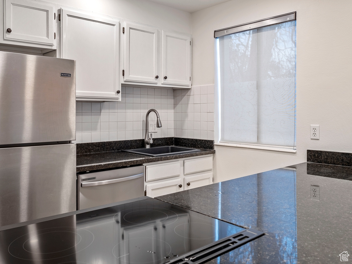 Kitchen featuring appliances with stainless steel finishes, tasteful backsplash, sink, dark stone countertops, and white cabinets