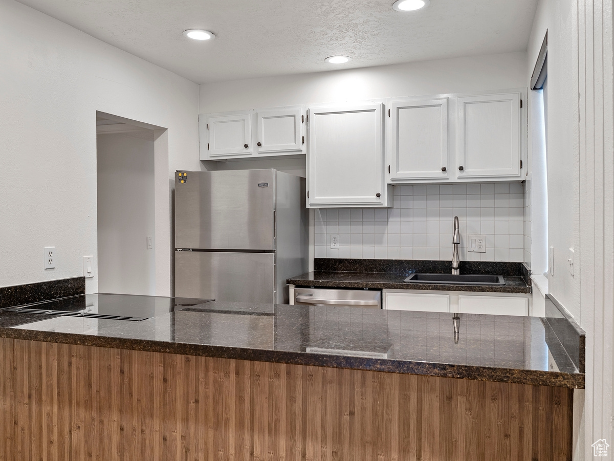 Kitchen with kitchen peninsula, stainless steel appliances, sink, dark stone countertops, and white cabinetry