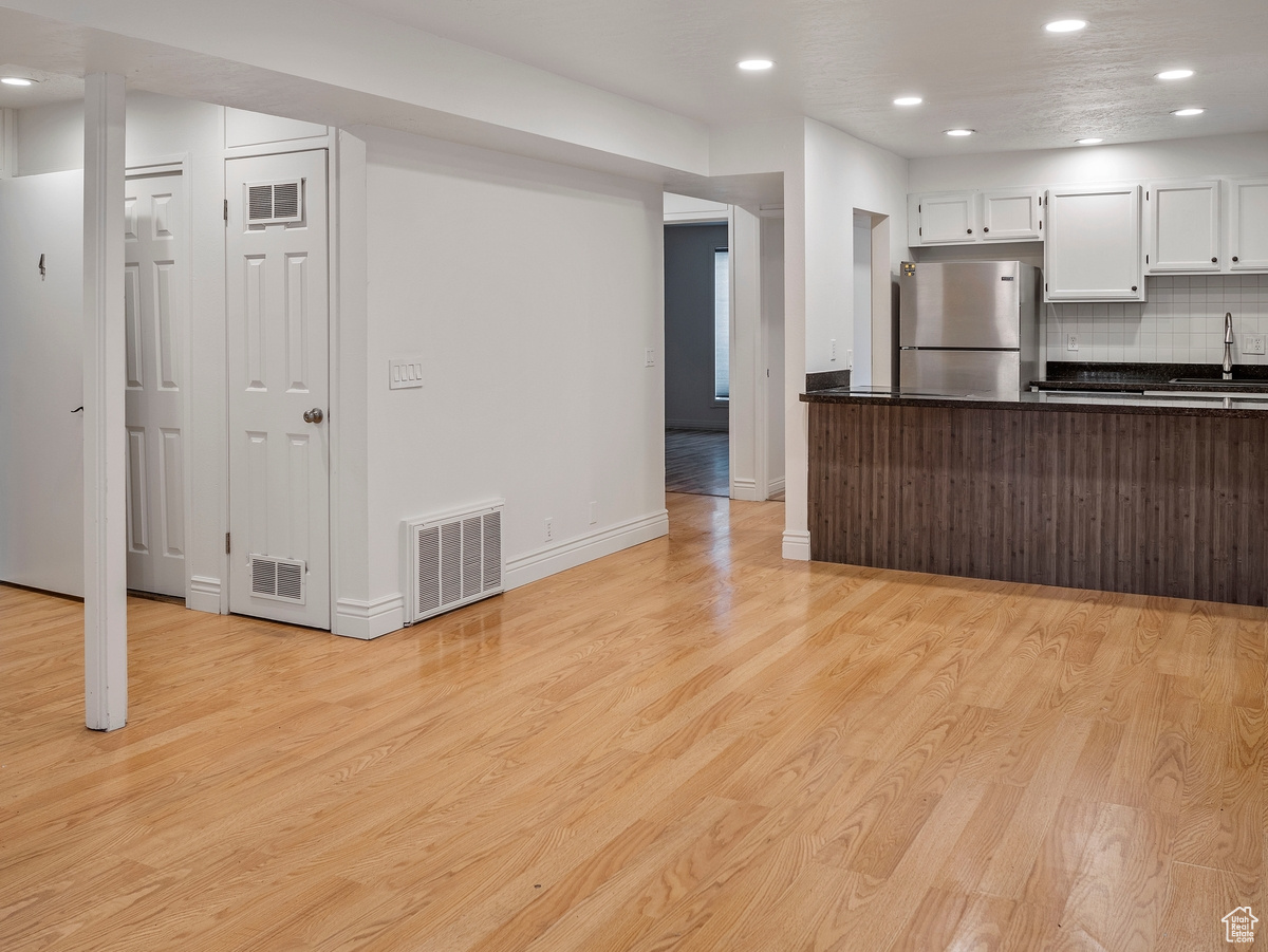 Kitchen featuring sink, tasteful backsplash, light hardwood / wood-style flooring, stainless steel fridge, and white cabinets