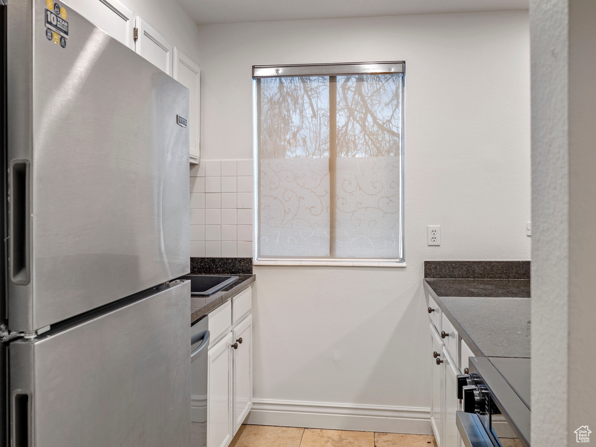 Kitchen with dark stone counters, white cabinets, light tile patterned flooring, and appliances with stainless steel finishes