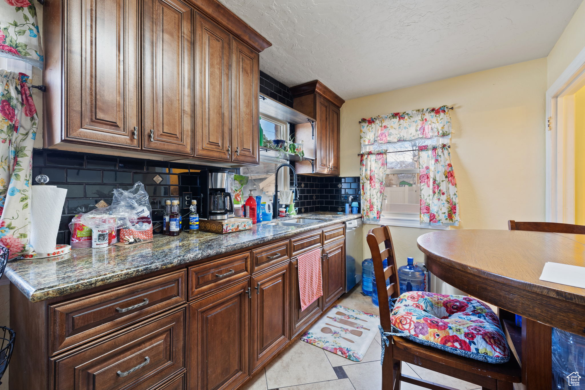 Kitchen featuring backsplash, a textured ceiling, sink, light tile patterned floors, and dark stone countertops