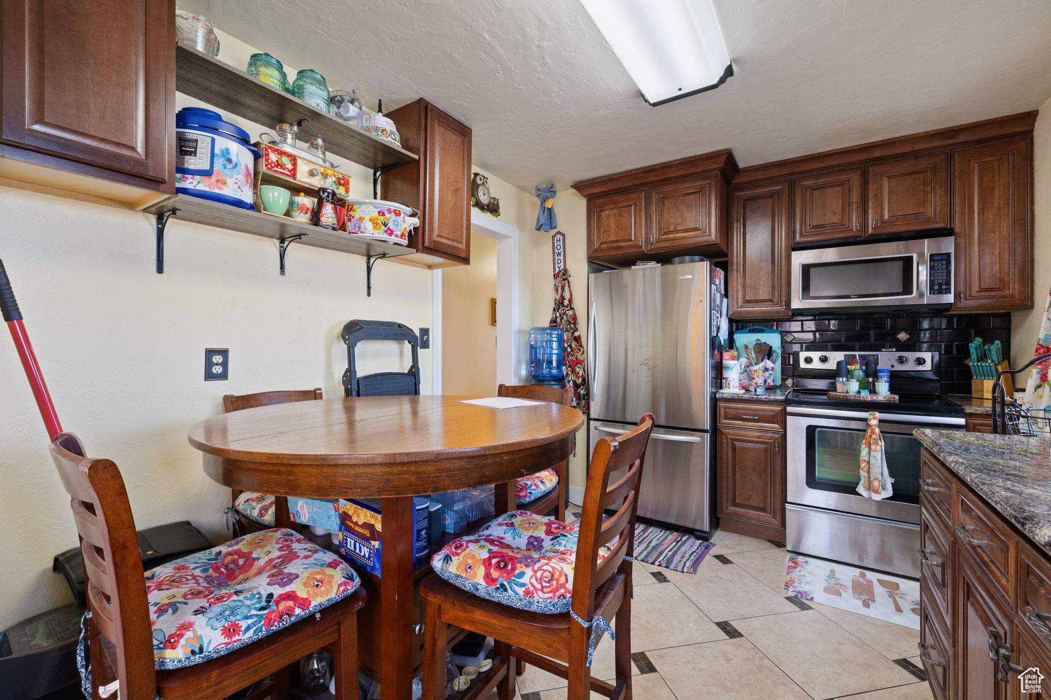 Kitchen featuring backsplash, dark stone counters, light tile patterned floors, a textured ceiling, and appliances with stainless steel finishes