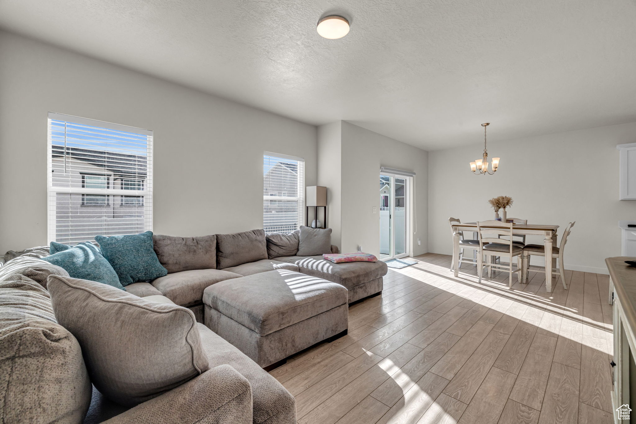 Living room with a healthy amount of sunlight, an inviting chandelier, a textured ceiling, and light hardwood / wood-style flooring