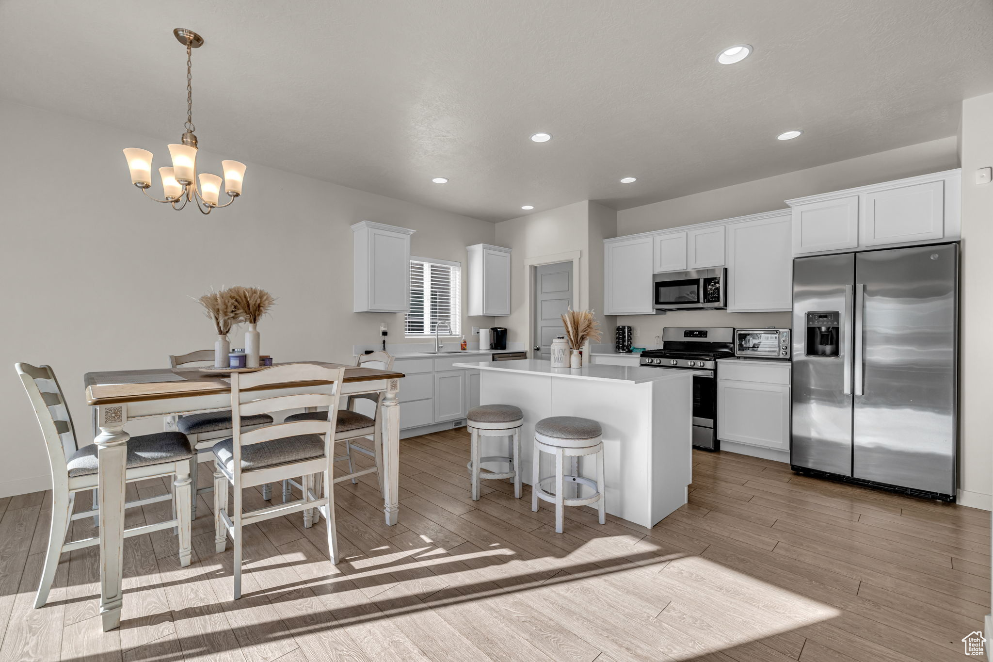 Kitchen with a center island, a notable chandelier, light hardwood / wood-style floors, white cabinetry, and stainless steel appliances