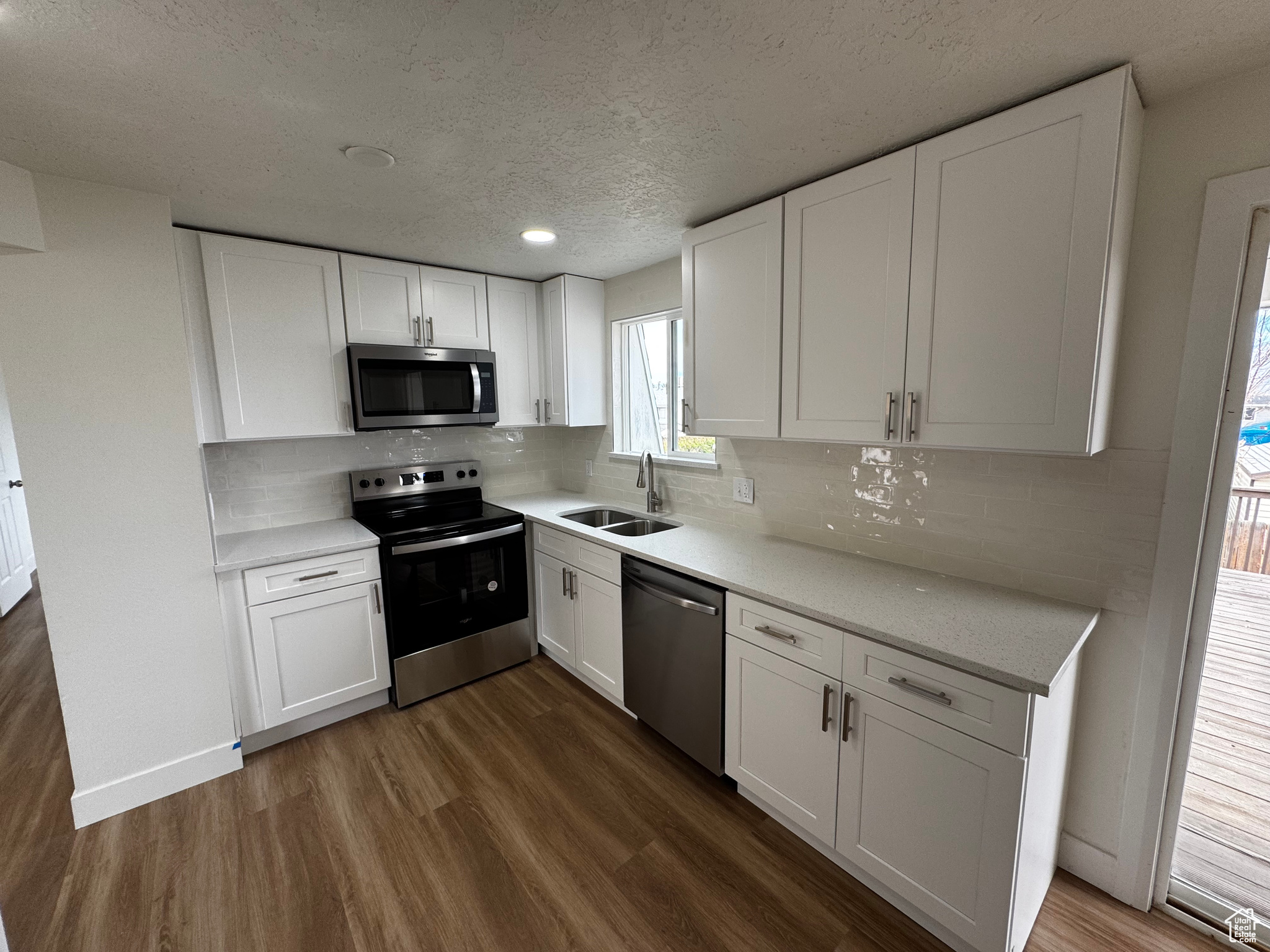 Kitchen with dark hardwood / wood-style flooring, tasteful backsplash, stainless steel appliances, sink, and white cabinets