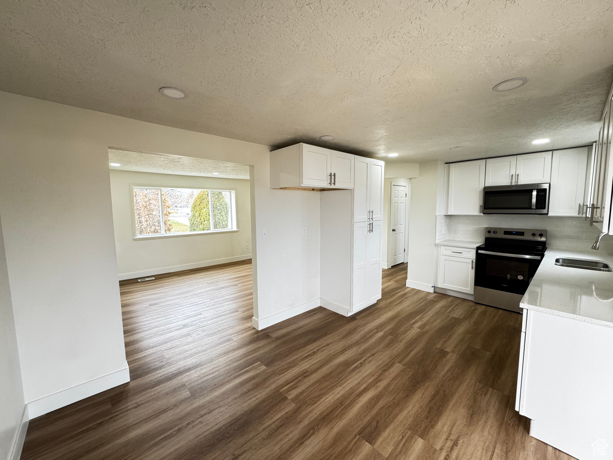 Kitchen with a textured ceiling, white cabinetry, stainless steel appliances, and dark hardwood / wood-style floors