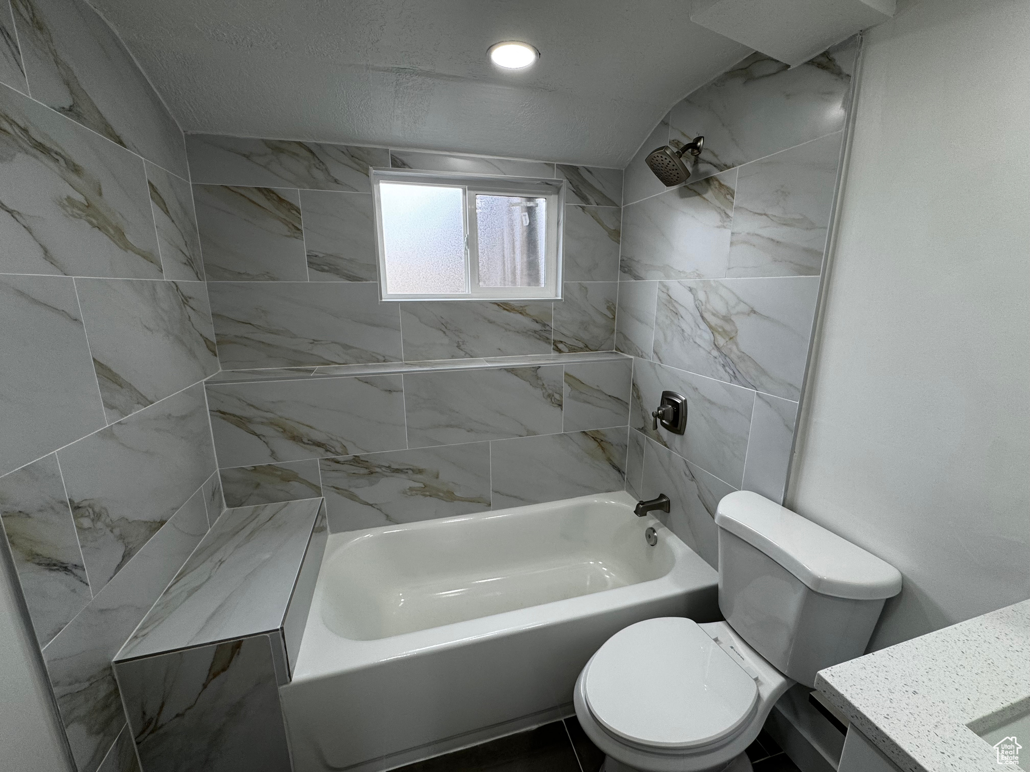 Full bathroom with vanity, lofted ceiling, tiled shower / bath combo, toilet, and a textured ceiling