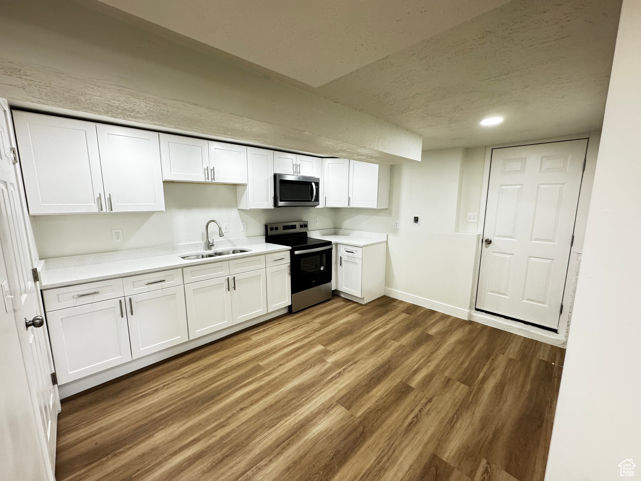 Kitchen featuring hardwood / wood-style flooring, sink, white cabinets, and appliances with stainless steel finishes